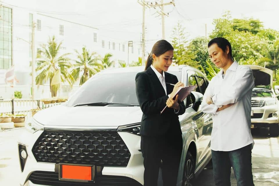 ผู้ชายกำลังตรวจรับรถป้ายแดงและสอบถามเรื่องประกันรถยนต์